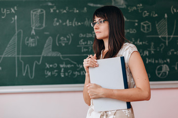 Woman teacher holding a study book and standing next a chalkboard. Back to school