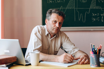 Teacher sitting in the classroom holding  a pen and looking at the camera Back to school