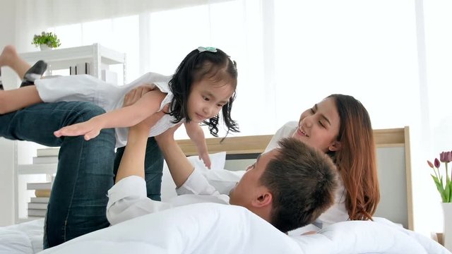 Asian family happy spending time together in the house. Daughter aged three playing with father on bed with open outstretched arms. Family leisure activities