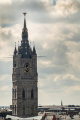 Fototapeta na wymiar Gent, Flanders, Belgium - June 21, 2019: Shot from castle tower, view over city roofs shows closeup of Belfry Tower against heavy white cloudscape with few blue patches.