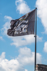 Gent, Flanders, Belgium -  June 21, 2019: Closeup of black-white-yellow-red flag of Gent City on top of castle tower against white cloudscape with blue patches.