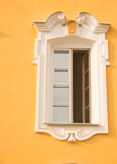 Window of an old building, palace. The frame is made of stucco in the Baroque style. White linen on a yellow background of the walls (ocher). Grand Peterhof Palace. Summer is a sunny day.