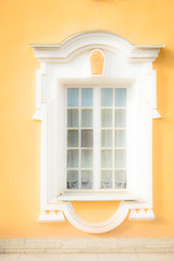 Window of an old building, palace. The frame is made of stucco in the Baroque style. White linen on a yellow background of the walls (ocher). Grand Peterhof Palace. Summer is a sunny day.