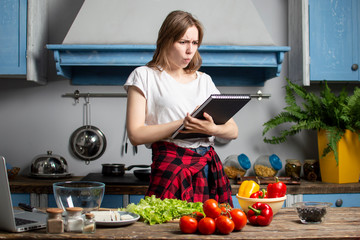 young girl prepares a vegetarian salad in the kitchen and looks into a recipe book, she learn to cook and reads