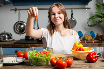 Obraz na płótnie Canvas young girl prepares a vegetarian salad in the kitchen, she adds sliced ingredients to the plate, the process of preparing healthy food