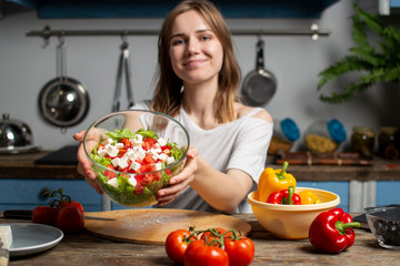 young girl prepares a vegetarian salad in the kitchen, holds a ready meal in her hands, the process of preparing healthy food