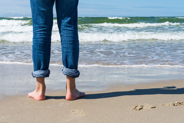 A teen boy stands on the sand facing the sea and sees off the summer. Concept. Summer is over. Seaside.