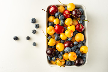 Fresh blueberries and cherries in a container, top view