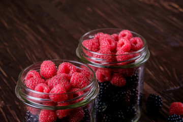 Raspberry and blackberry sweet organic juicy berries in two glass jars on dark wooden table