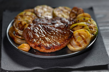 tasty grilled pork meat with vegetable on plate over black napkin
