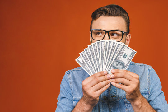 Image of shocked excited young handsome bearded man posing isolated over orange wall background holding money make winner gesture.
