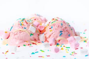 pink berry scoops ice cream strewed sprinkles, marshmallows and icing on white background
