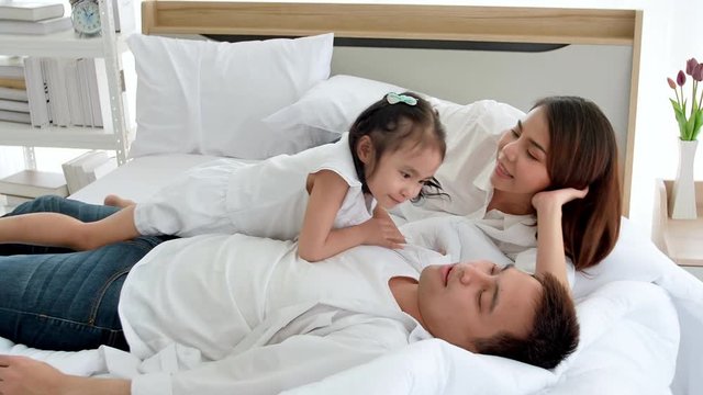 Asian family happy spending time together on the bed in the house. Daughter aged three kissing cheeks parents.