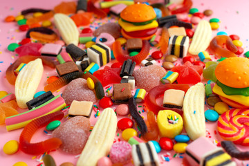 mixed colorful sweet candies with jelly and sprinkles over pink festive background