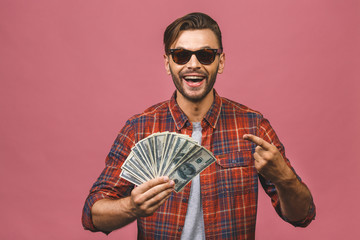 Image of shocked excited young handsome bearded man posing isolated over pink wall background holding money make winner gesture.