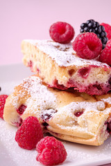 Homemade piece of cake, two pie slices with raspberry and blackberry berries, powdered sugar, in white square plate on pink paper background, macro, close up