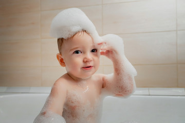 Baby with soap foam or shampoo on his head. Cute baby swims in the bathtub with lots of foam
