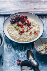 Healthy oatmeal breakfast with red currants, raspberry, grape and boiled egg with toast and coffee on a rustic blue background