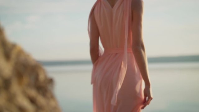 A girl in a white summer dress stands in the spray of the Mediterranean sea near the rock of Aphrodite. A girl in a beautiful summer dress near the rocks on the background of water
