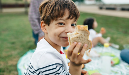 Portrait of smiling boy holding sandwich with his family in background