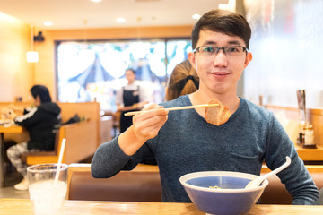 Asian man using bamboo chopsticks for eating sliced pork in restaurant