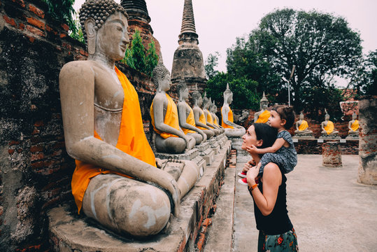 Thailand, Bangkok, Ayutthaya, Buddha statues in a row in Wat Yai Chai Mongkhon, mother and daughter in front of a buddha statue
