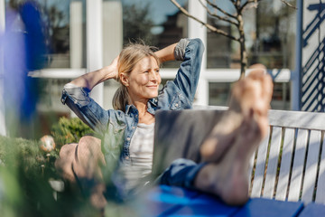 Smiling woman with laptop relaxing on garden bench