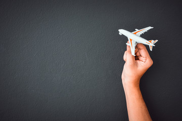 man's hand holding white toy airplane model over black color wall background with copy space, concept of travel