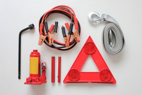 Basic emergency kit for a car consisting of a bottle jack,wheel spanner,tow rope,red triangles,and jumper cables.