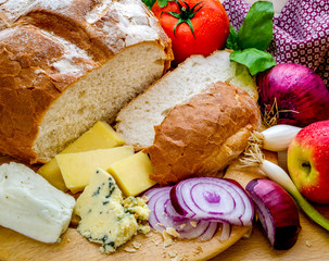 A horizontal shot of a delicious quick snack of a ploughman&rsquo;s lunch with fresh bread a variety of cheese and a fresh tomato and an apple. 