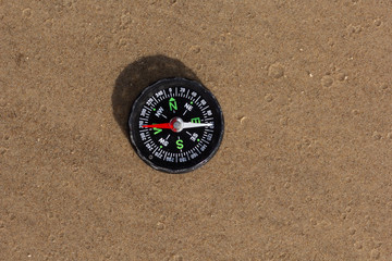 Fototapeta na wymiar Compass pointing West laying on sand beach