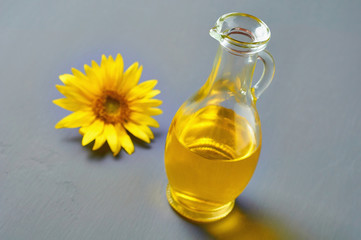 Beautiful blossoming sunflower with yellow leaves near glass jug of oil on gray concrete