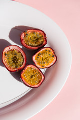 Fresh passion fruit on ceramic plate on a pastel pink background in top view. Ripe tropical passion fruit close up. Dessert of Vegetarian diet. intermittent fasting diet. Healthy snack.