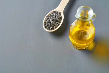 Full wooden spoon of sunflower seeds near jug with oil on gray concrete. Space for text