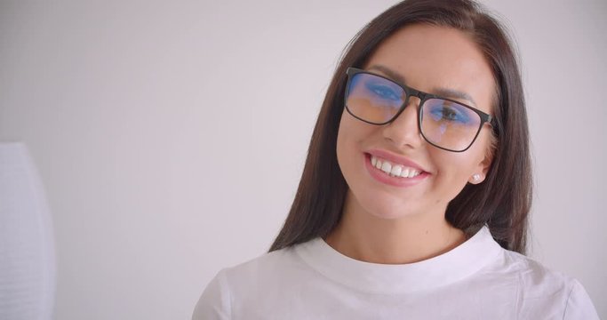 Closeup portrait of young pretty caucasian businesswoman in glasses looking at camera smiling cheerfully with white background