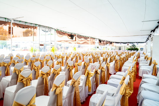 Temporary Air Conditioner Indoor Tent For Outdoor Event In The Day. Inside Tents Has Red Carpet And A Lot Of Chair Covered By White Cloth And Golde Ribbon On It.