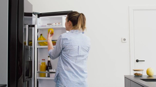 healthy eating, food and diet concept - happy woman opening fridge and taking apple at home kitchen