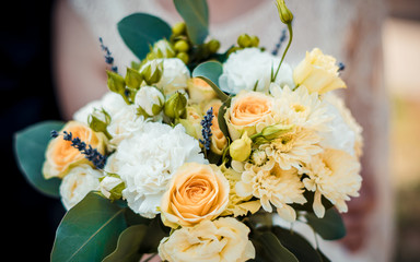 Wedding bouquet of orange flowers with blue leaves in the hands of the bride