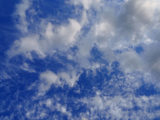 Landscape of blue sky covered with light thin fluffy white clouds and a thundercloud coming from the up right with the sun illuminates part of the clouds. Cloudscape bottom up view. 