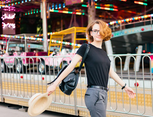 Young cheerful hipster woman in glasses and hat in amusement park
