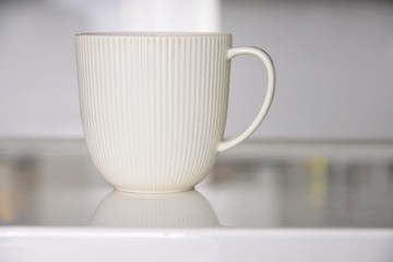 Elegant beige porcelain tea cup with a textured surface with selective focus on blurred neutral background. Coffee time. Ceramic mug with exquisite design for morning tea time. White teacup on table 