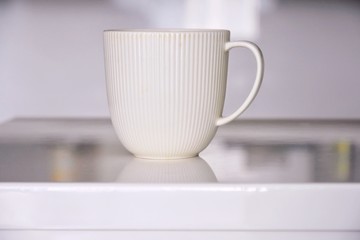 Elegant beige porcelain tea cup with a textured surface with selective focus on blurred neutral background. Coffee time. Ceramic mug with exquisite design for morning tea time. White teacup on table 