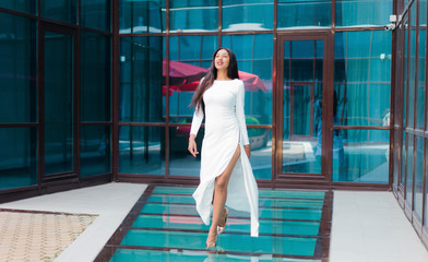 Fototapeta na wymiar Beauty afro woman in a luxurious white dress walking against building with blue windows