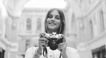 Happy tourist woman with a retro camera in her hands while posing at urban old architecture. Discover new places