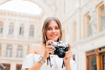 Young attractive tourist woman with a retro camera in her hands while posing at urban old architecture. Discover new places