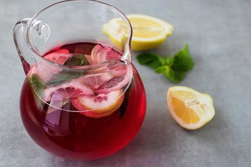A refreshing drink of hibiscus, mint and lemon in a glass jug on a gray background. Soft focus.