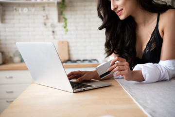 cropped view of sexy girl in black underwear and white shirt using laptop and holding credit card