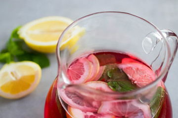 A refreshing drink of hibiscus, mint and lemon in a glass jug on a gray background.