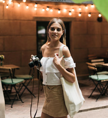 Beauty blond woman in fashionable clothes holding retro camera in evening on the background of...