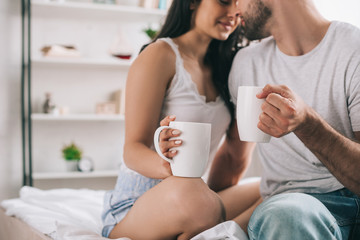 cropped view of man and woman holding cups with tea and kissing